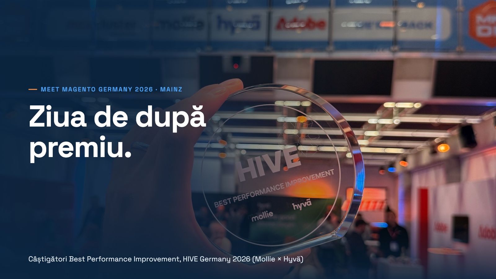 O mână ține sus trofeul de sticlă HIVE, gravat Best Performance Improvement, Mollie și Hyvä, în zona expozanților din Pyramide Mainz, sub bannerele sponsorilor Meet Magento Germany. Text: Meet Magento Germany 2026, Mainz. Ziua de după premiu. Câștigători Best Performance Improvement, HIVE Germany 2026 (Mollie × Hyvä).