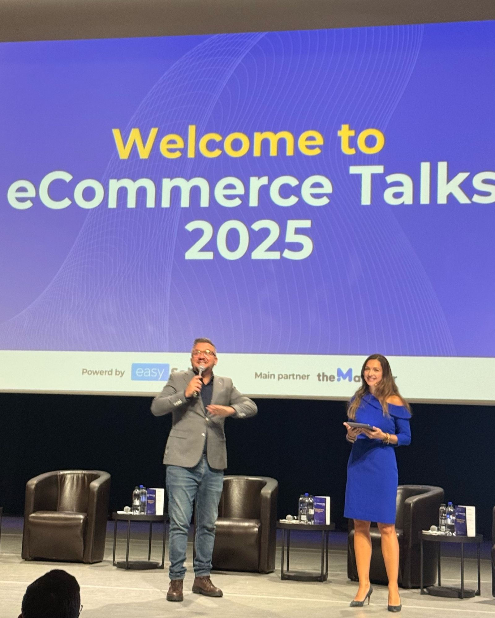 The hosts open eCommerce Talks 2025 on the Aula Magna stage, under the “Welcome to eCommerce Talks 2025” slide.