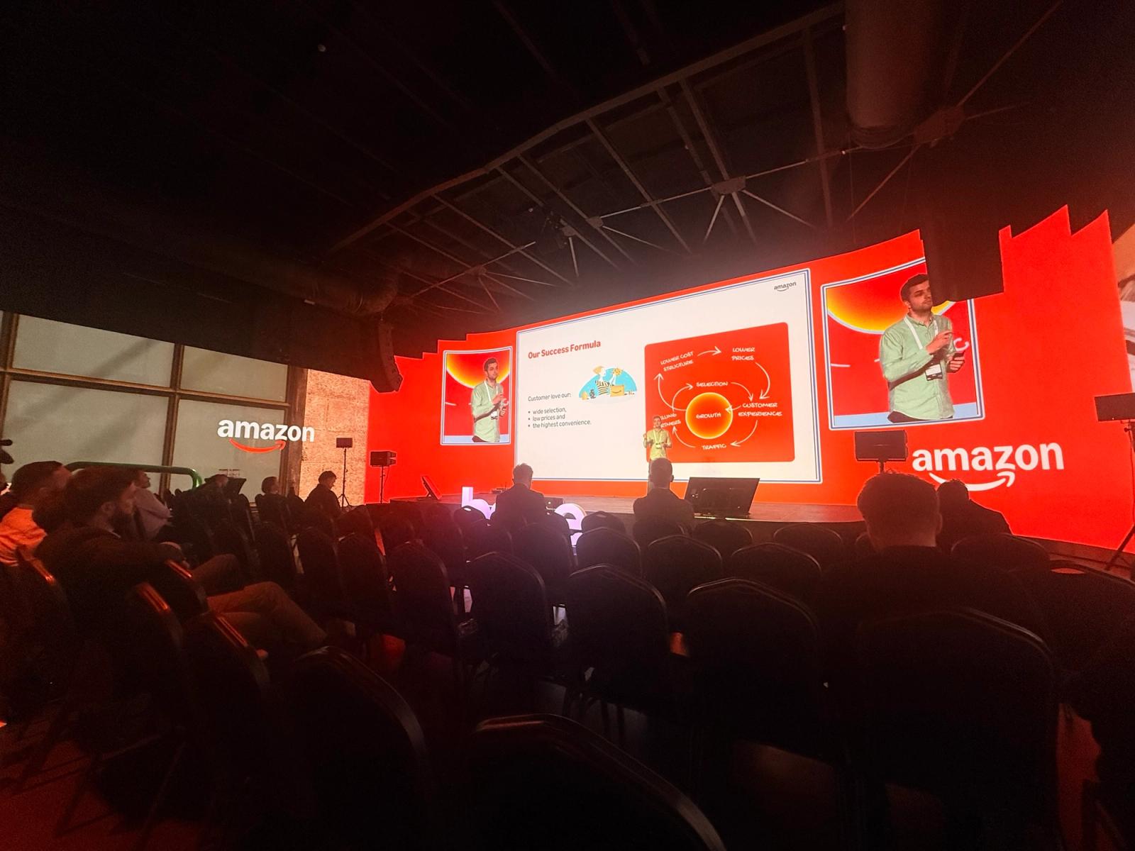 Amazon's talk at The Base Event 2026, with the "Our Success Formula" slide and its growth flywheel: lower prices, customer experience, traffic, selling partners, selection.