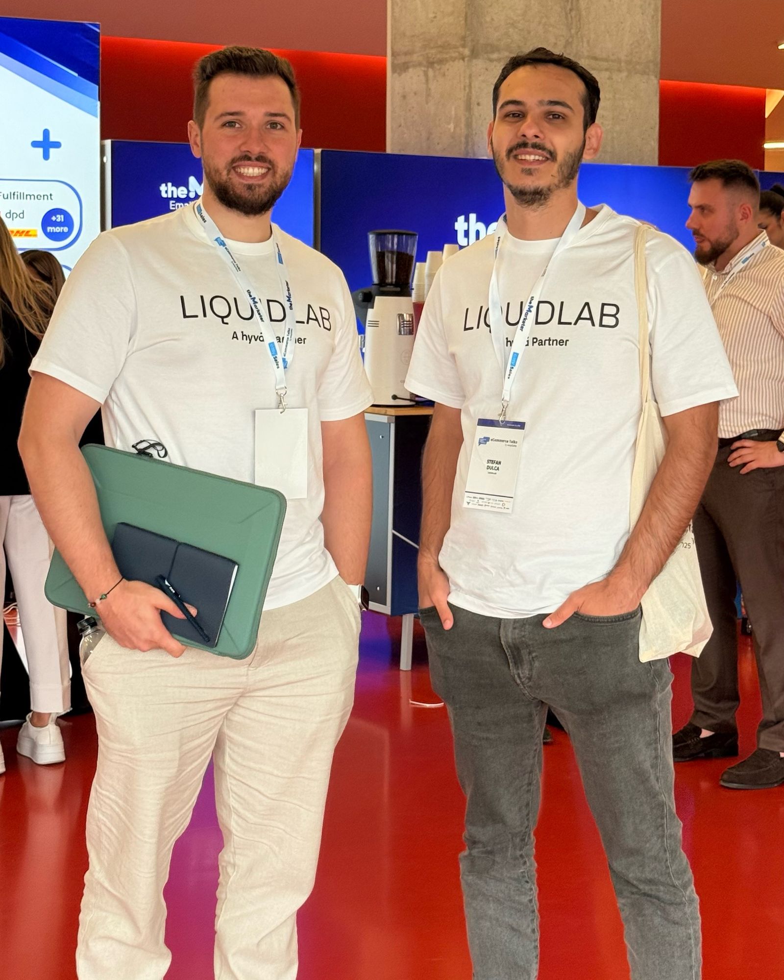 Two members of the LIQUIDLAB team in “LIQUIDLAB, A Hyvä Partner” T-shirts in the eCommerce Talks 2025 foyer.