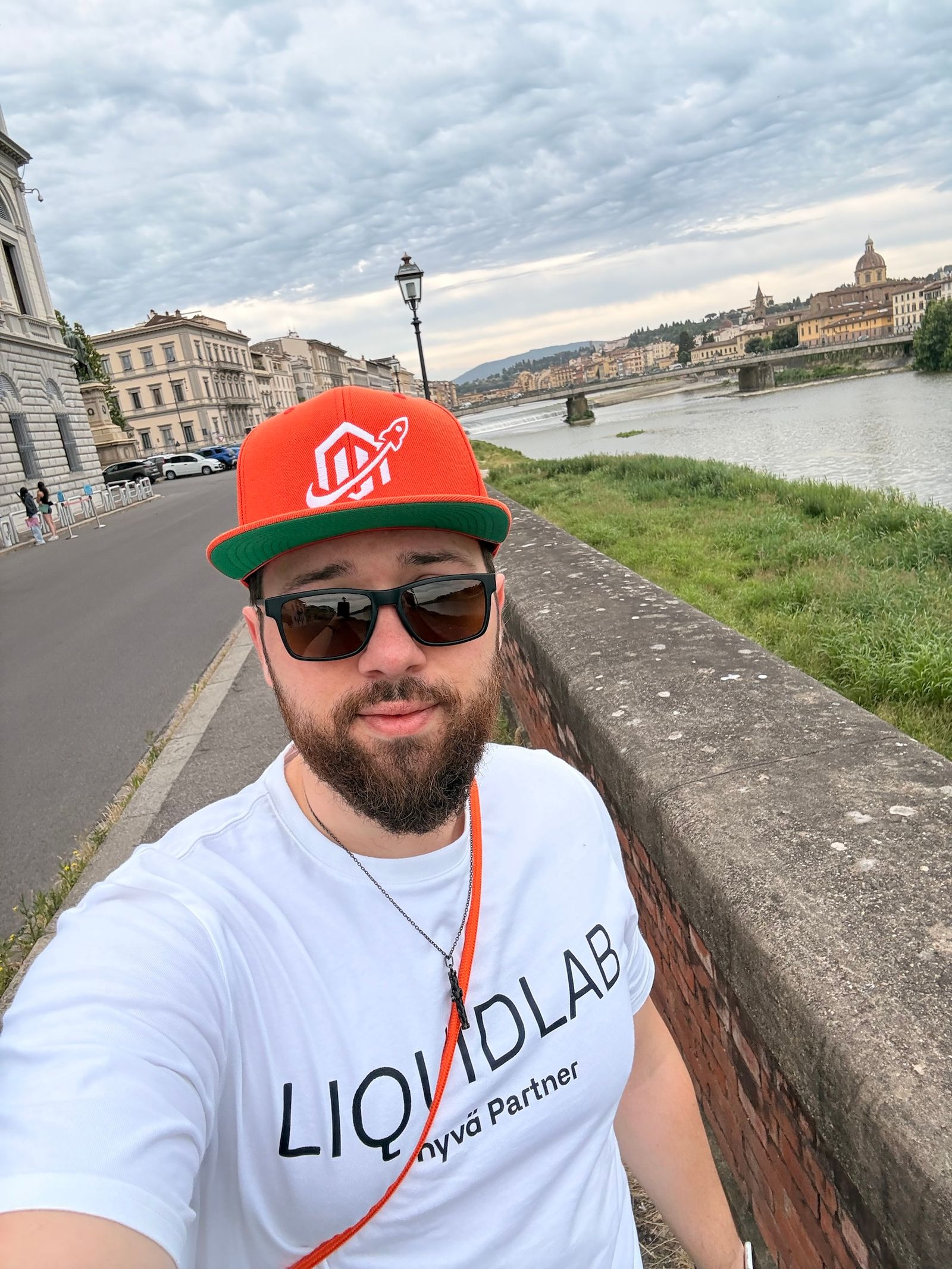 Alexandru-Manuel Carabus of LIQUIDLAB on the Lungarno in Florence on the morning of Meet Magento Italy 2026, wearing a LIQUIDLAB t-shirt and a red cap.