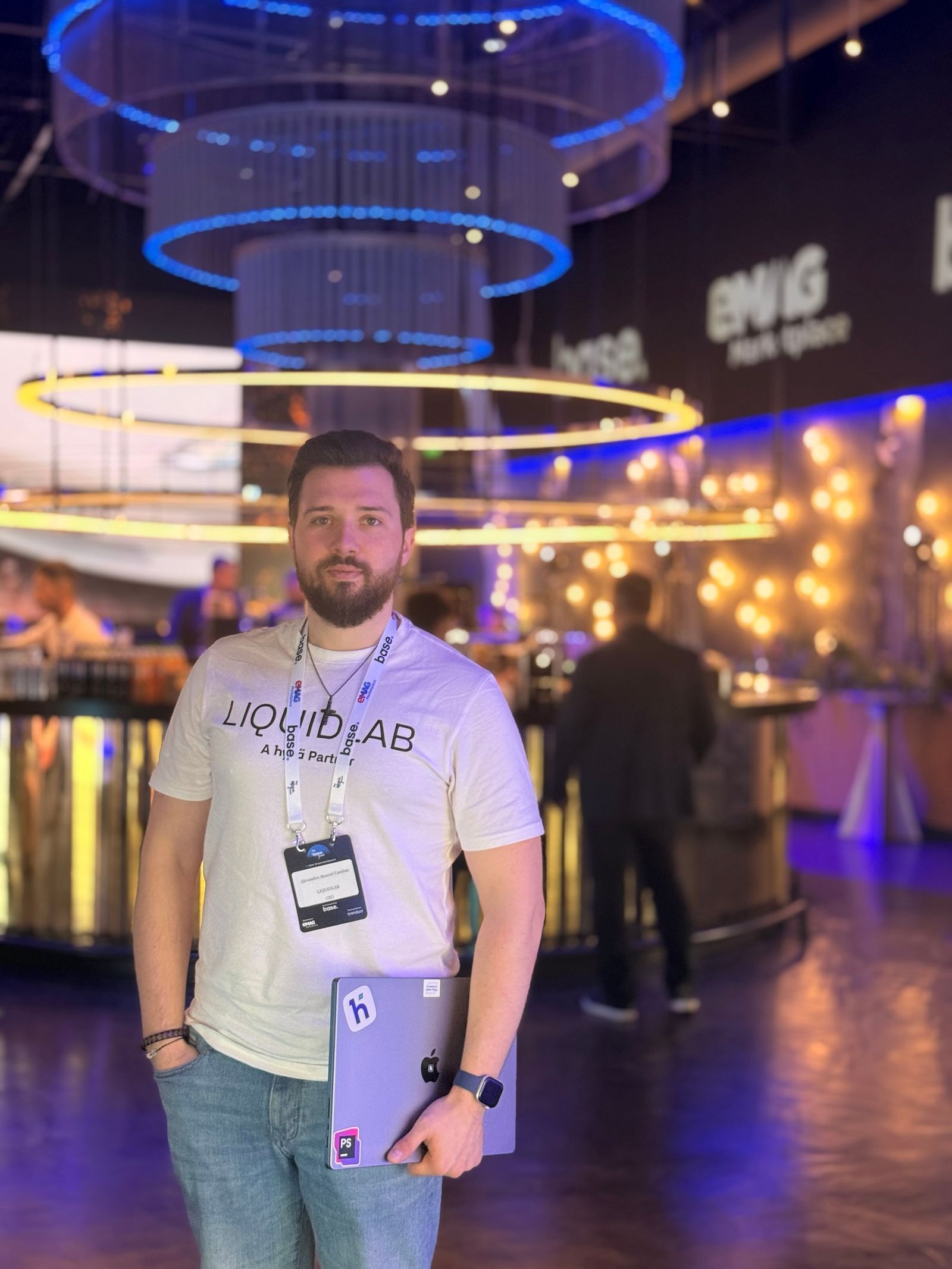 The LIQUIDLAB founder in the "LIQUIDLAB, A Hyvä Partner" T-shirt with The Base Event badge, in the networking area at HALO.