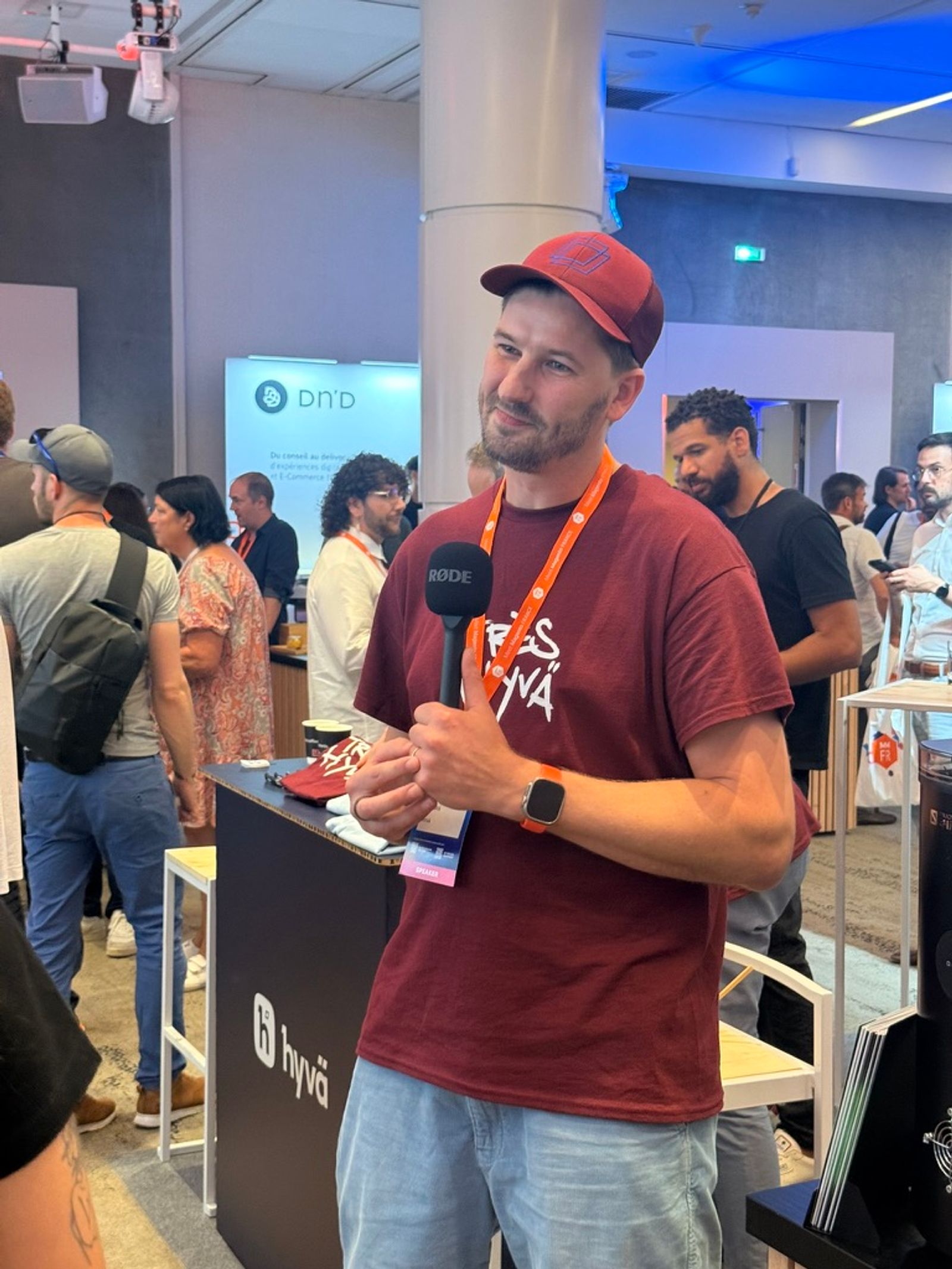 An attendee wearing a Yes Hyvä t-shirt being interviewed with a RØDE microphone at the Hyvä sponsor stand at MM France 2026.
