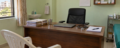 A doctor's desk in a small Indian clinic with patient files, a prescription pad, a stethoscope and a closed laptop