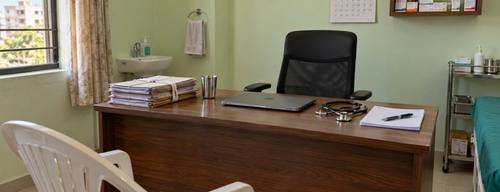A doctor's desk in a small Indian clinic with patient files, a prescription pad, a stethoscope and a closed laptop