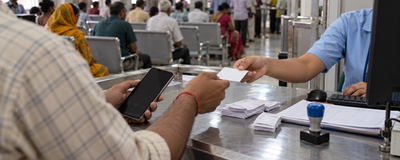 A patient handing a printed card and a phone across a hospital registration counter to a receptionist at a computer