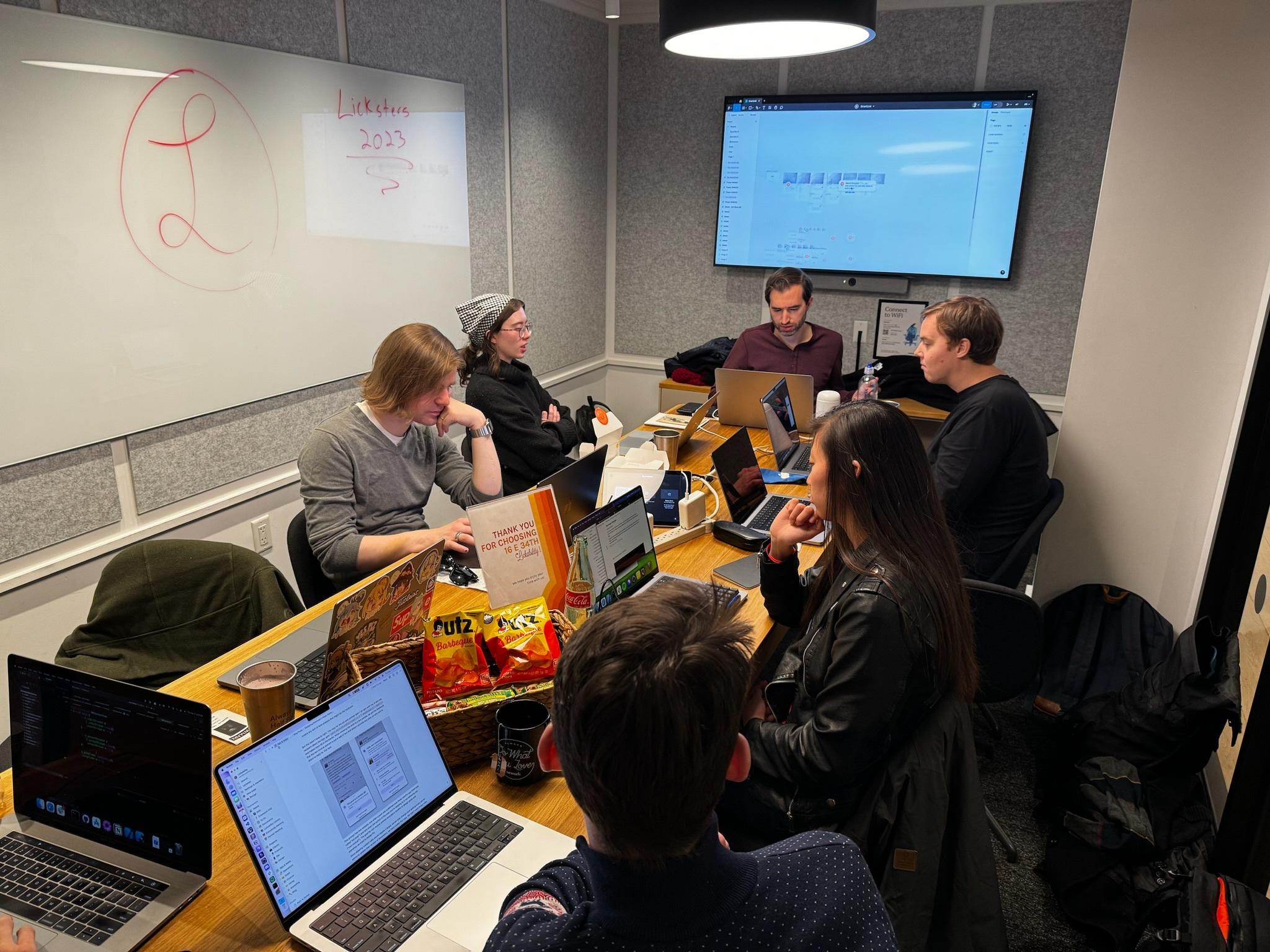 The Lickability team sitting around a conference table in a WeWork office. The whiteboard has a hand-drawn version of our logo with the words “Licksters 2023."