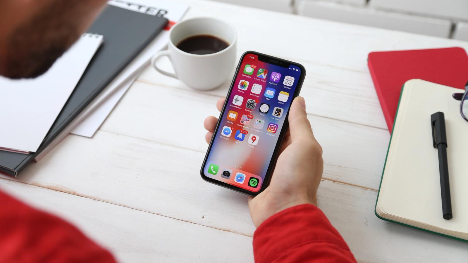 A person's hand holding an iPhone, with lots of apps on the home screen.