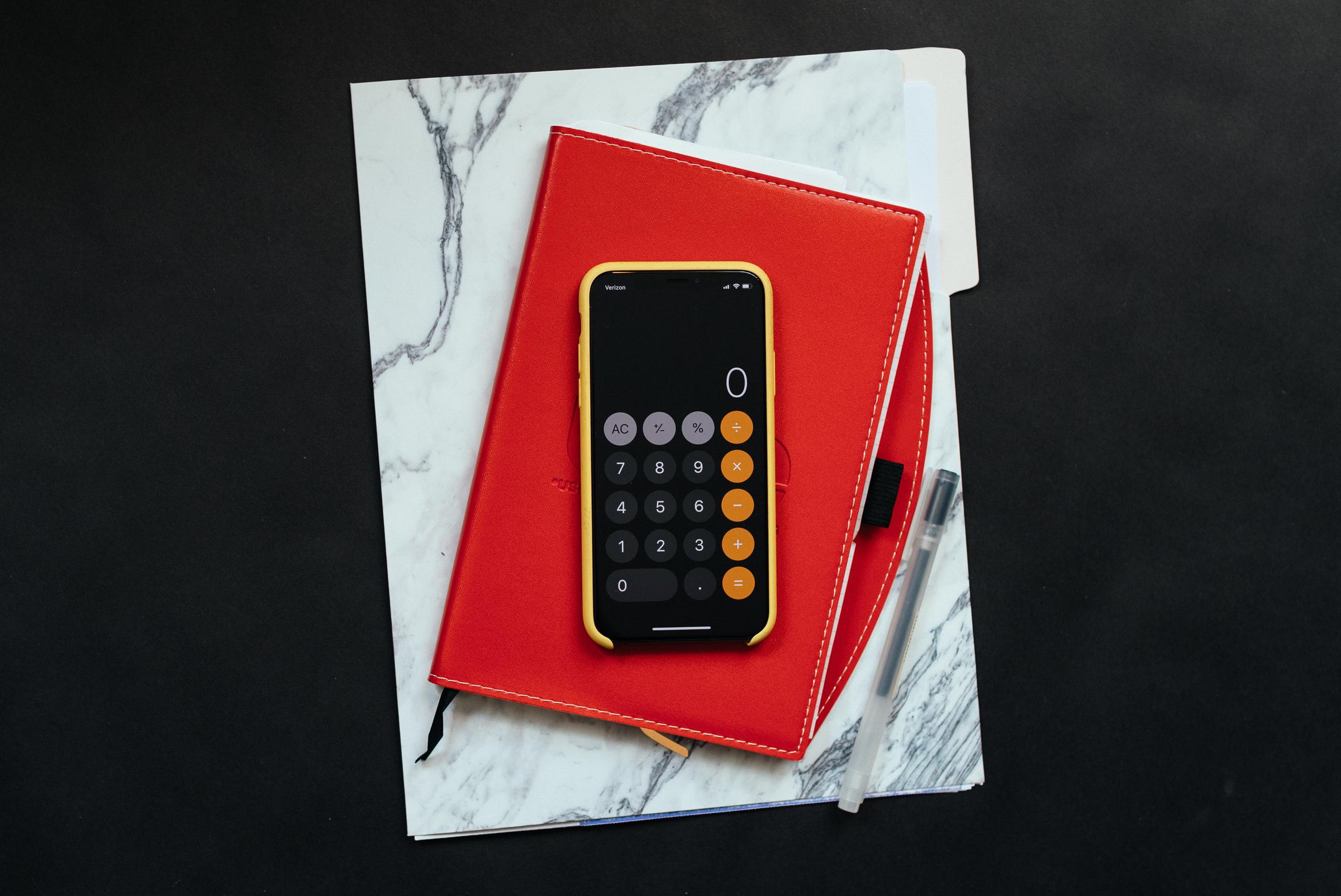 A red notebook and iPhone with the calculator app open.