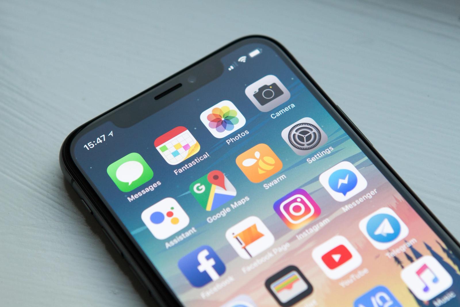 An iPhone sitting on a table, showing the Home Screen with a grid of app icons