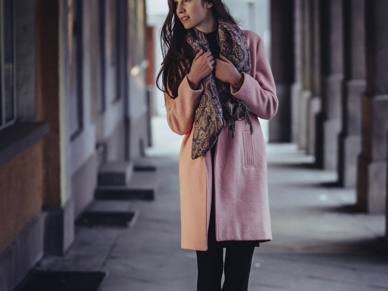 Woman in a pink coat walking through a stone arcade