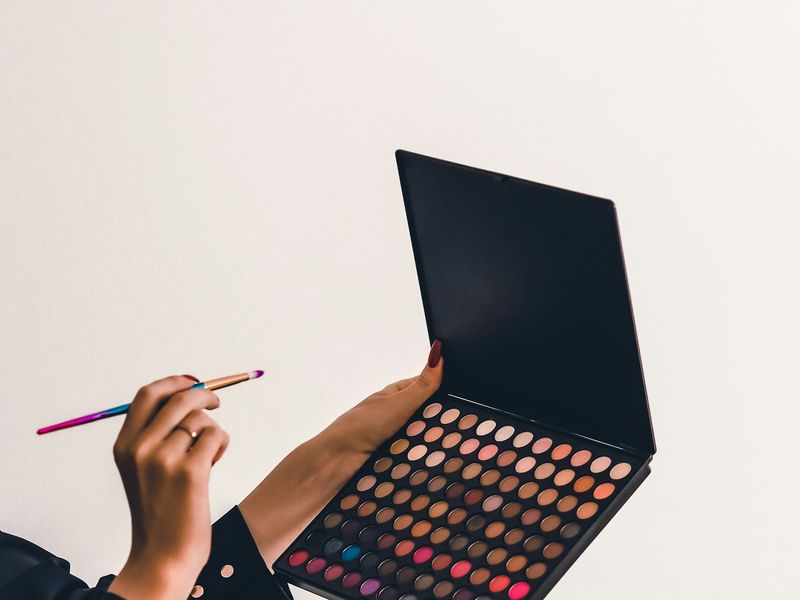Hand holding a brush over an open eyeshadow palette