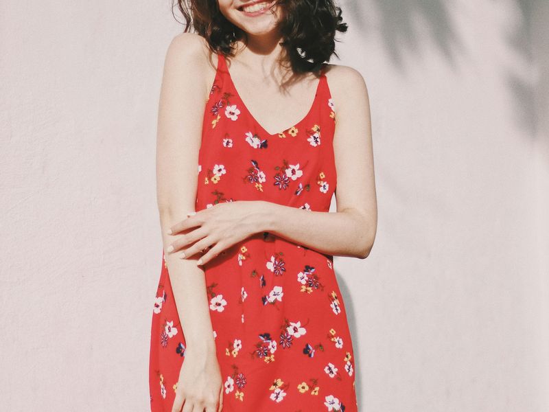 Woman in a red floral slip dress against a pale wall