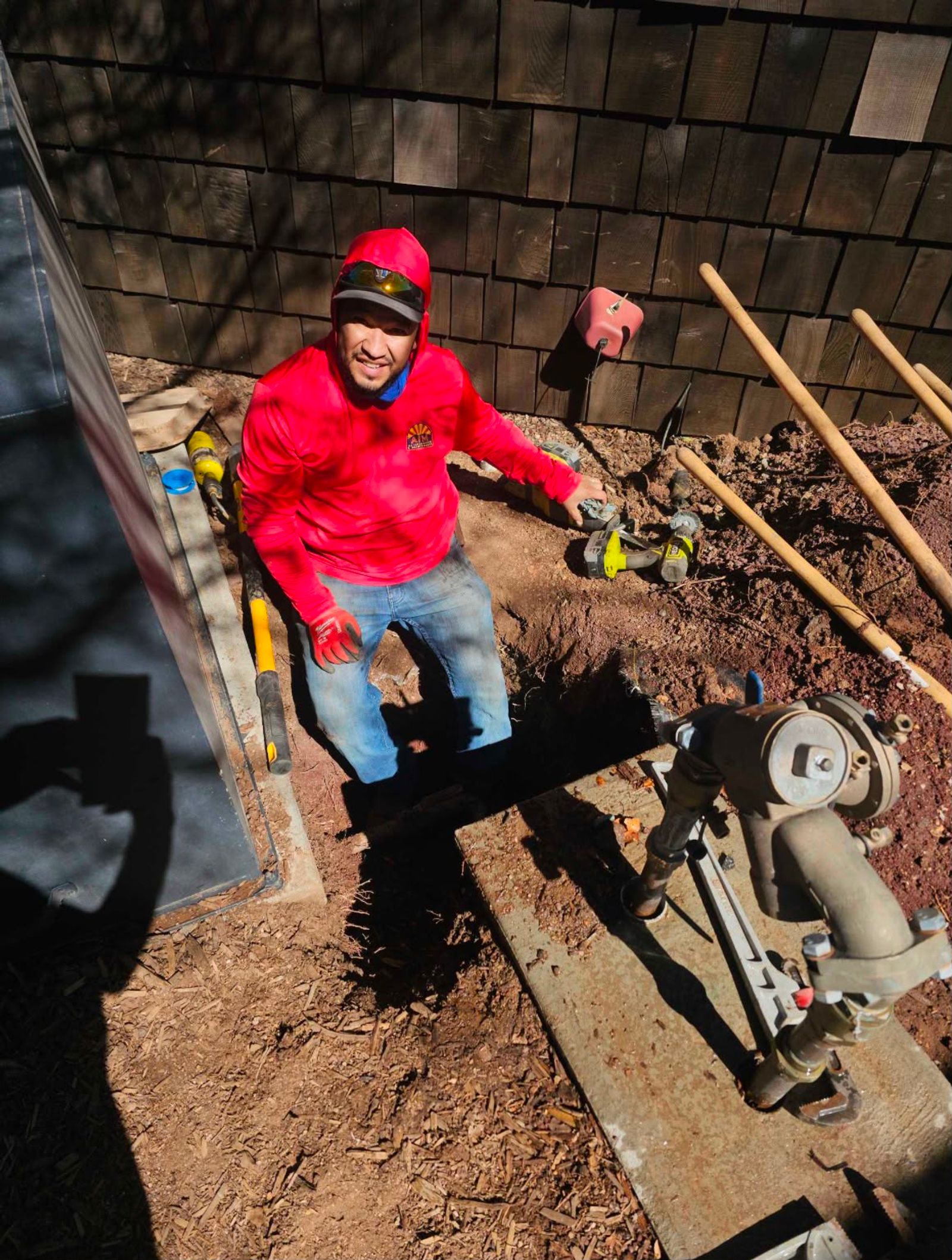 An AZ Irrigation & Maintenance technician kneeling beside an excavated irrigation line and backflow assembly