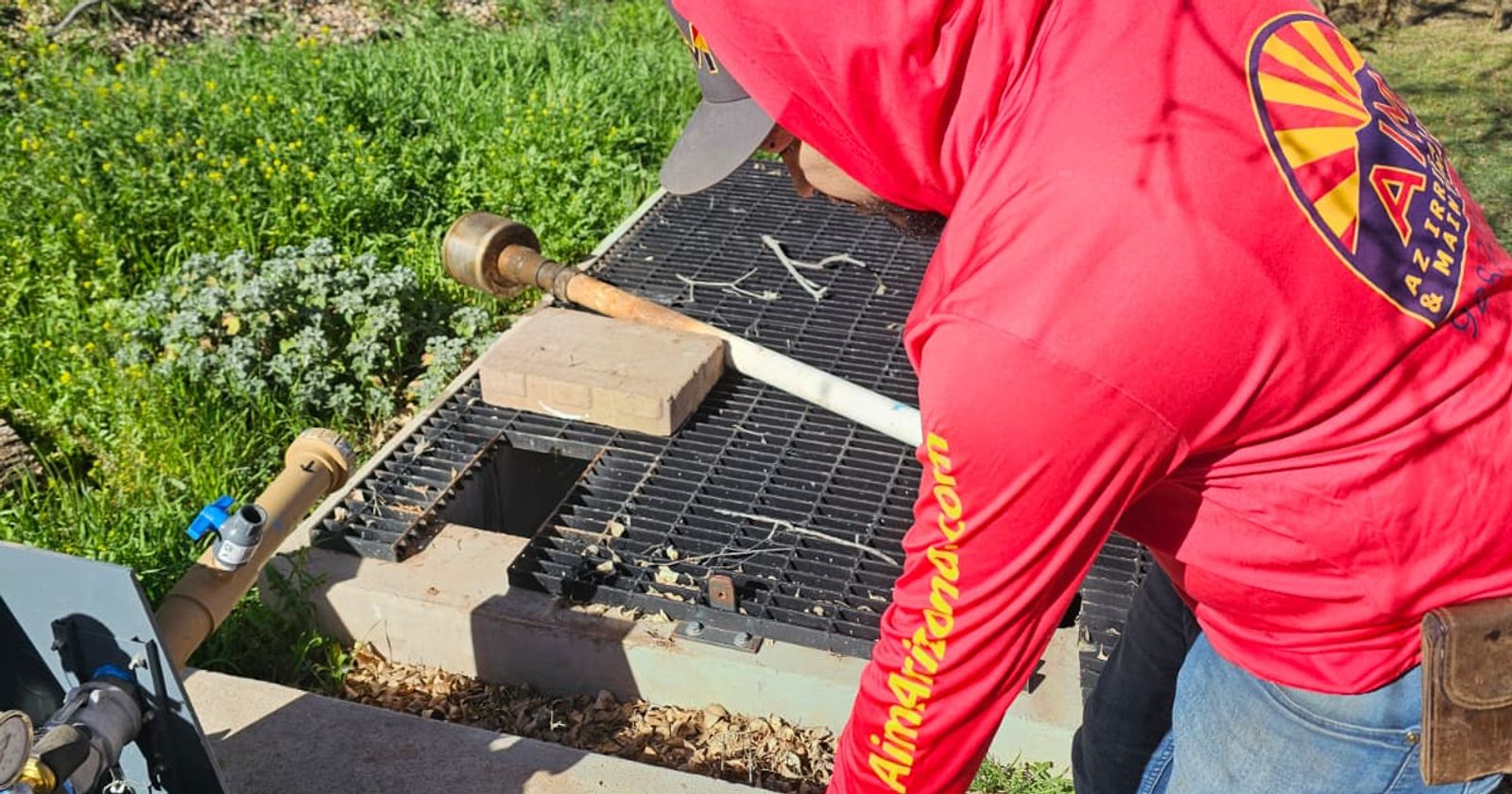 An AZ Irrigation technician opening a valve box and testing the brass valve assembly with a cordless driver