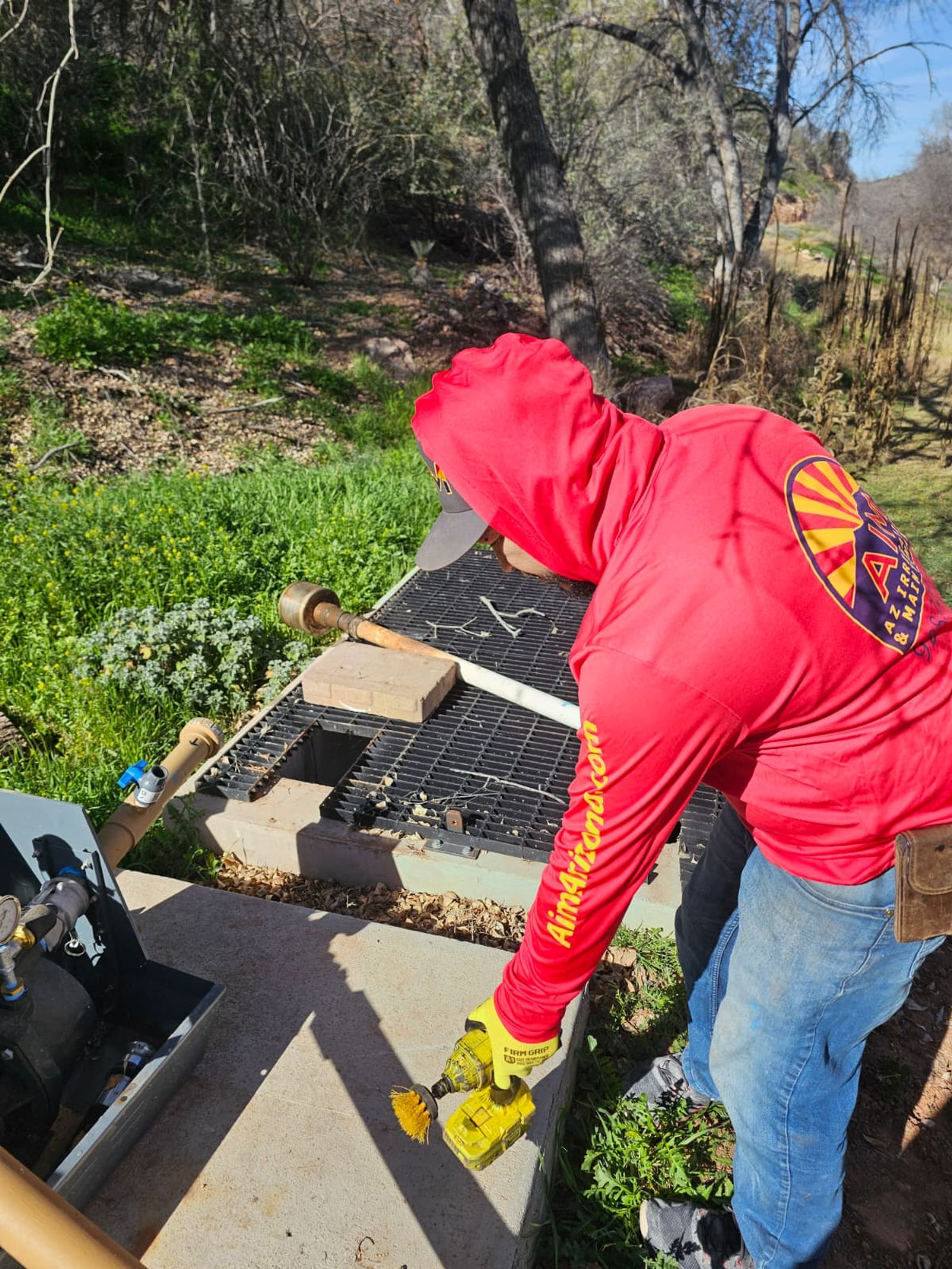 An AZ Irrigation technician opening a valve box and testing the brass valve assembly with a cordless driver