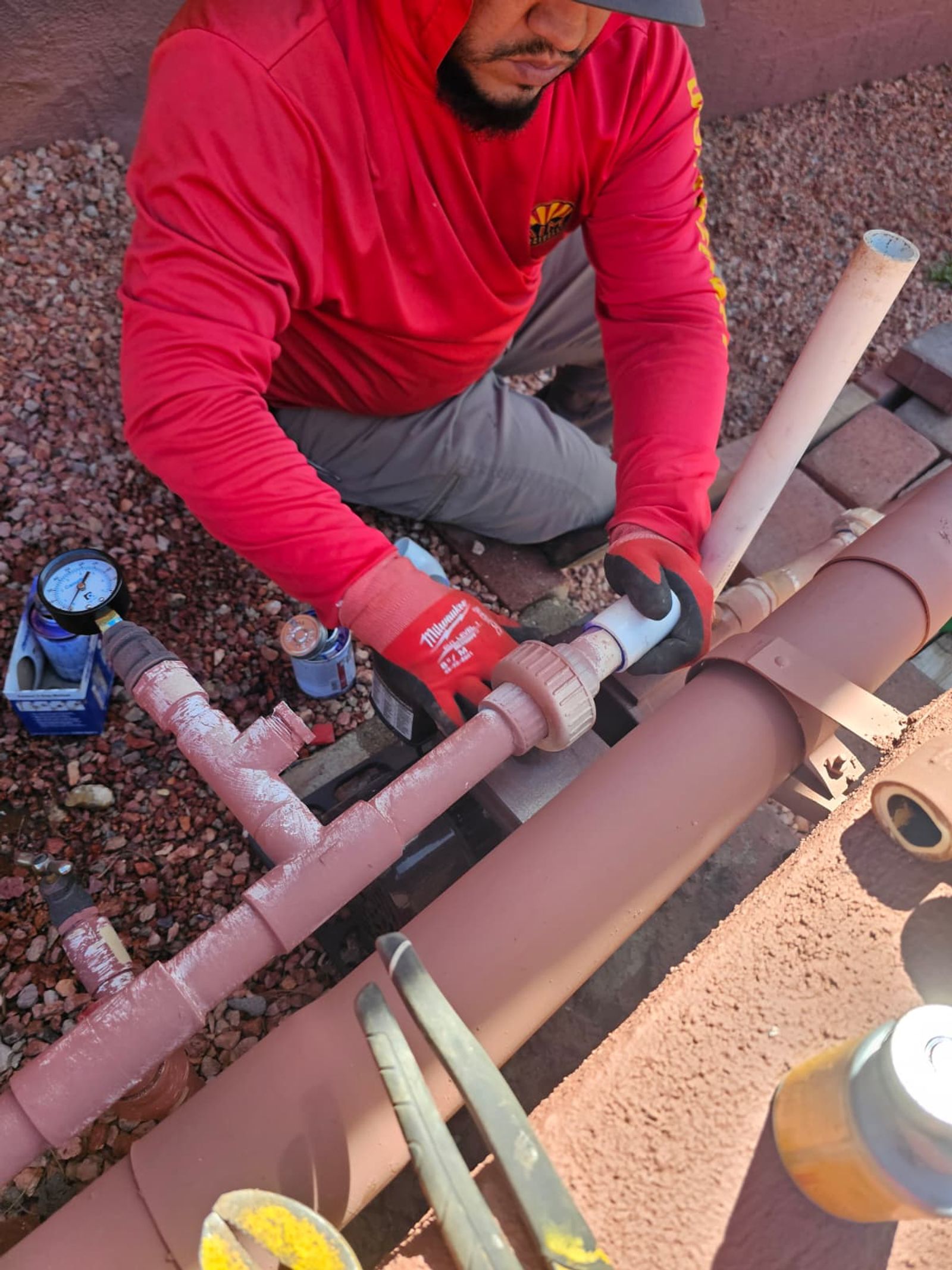 An AZ Irrigation technician assembling and solvent-welding a PVC irrigation manifold beside a pressure gauge