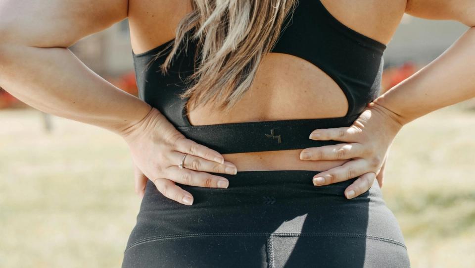 A person in activewear holding their lower back, illustrating lower back pain and mattress support