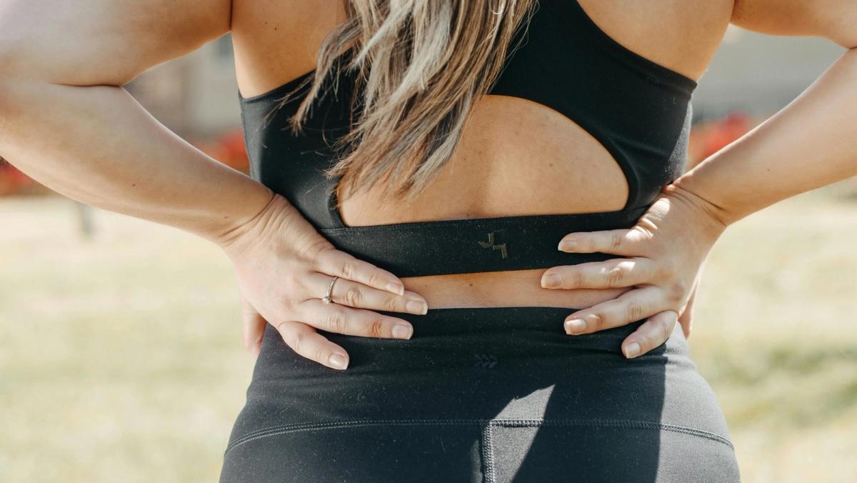 A person in activewear holding their lower back, illustrating lower back pain and mattress support