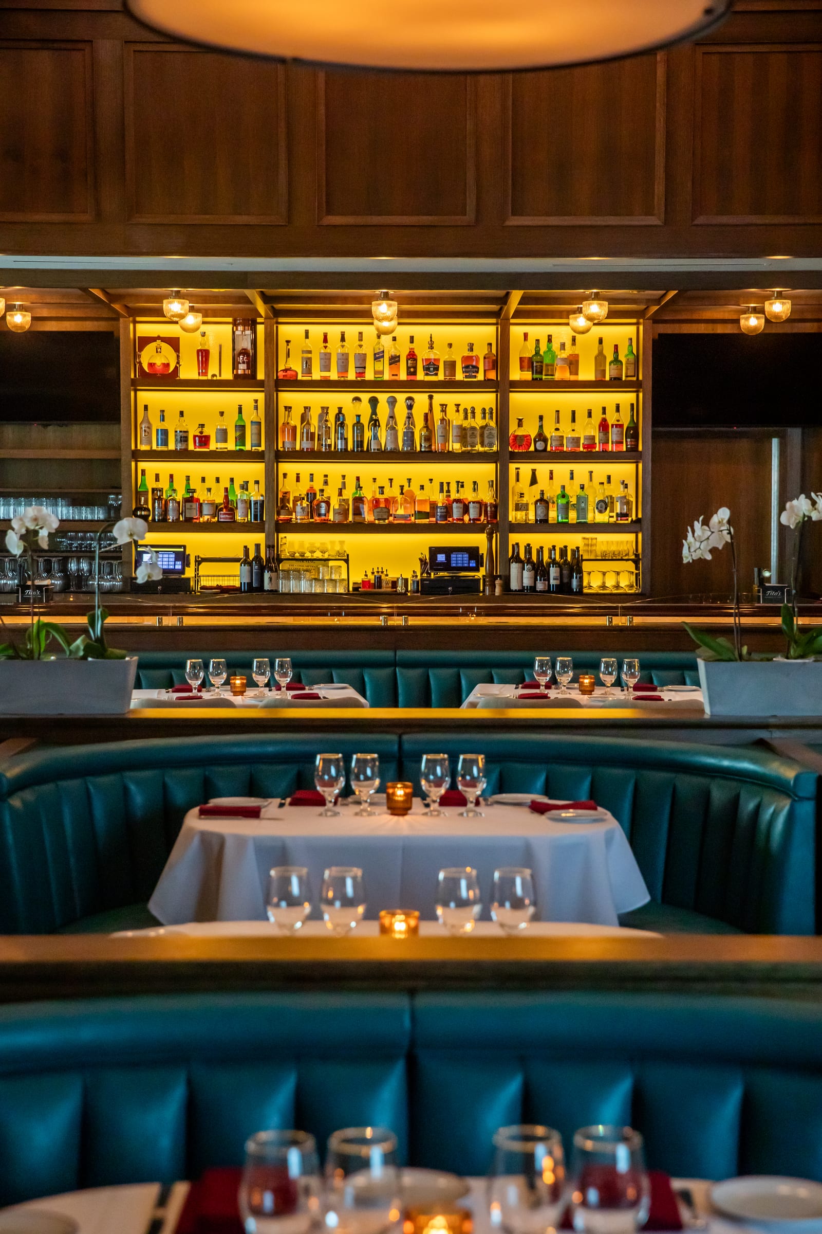 Backlit amber bar shelves rising above a teal corner booth