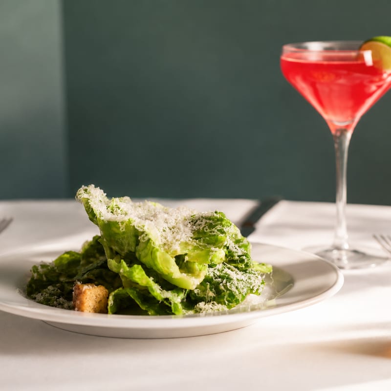A parmesan-dusted Caesar salad beside a crimson cocktail