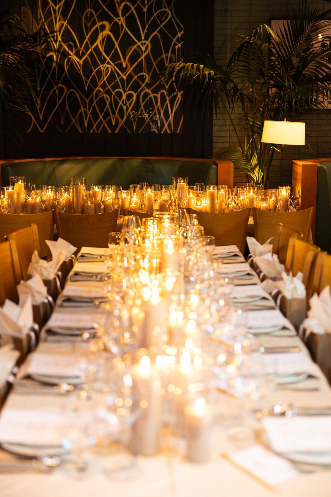 Candlelit private dinner table set for a party, heart-motif mural and palms behind