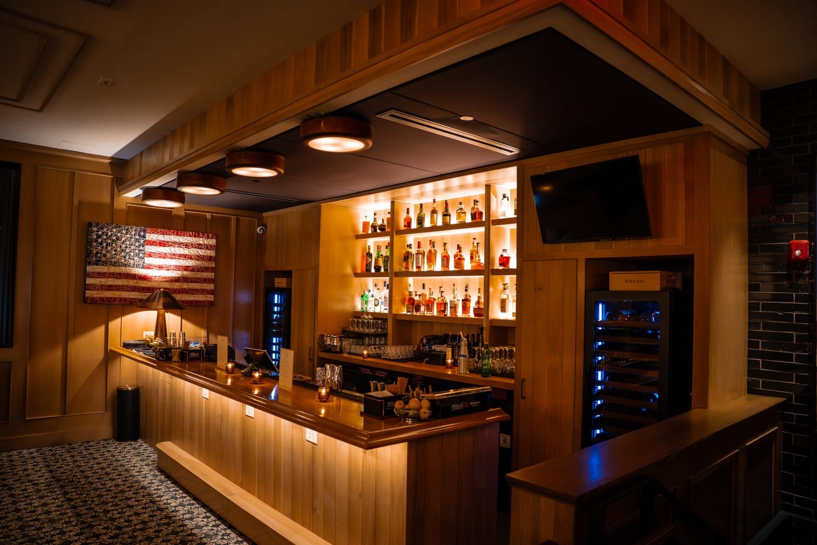 Warm wood bar with backlit spirit shelves and an American flag artwork
