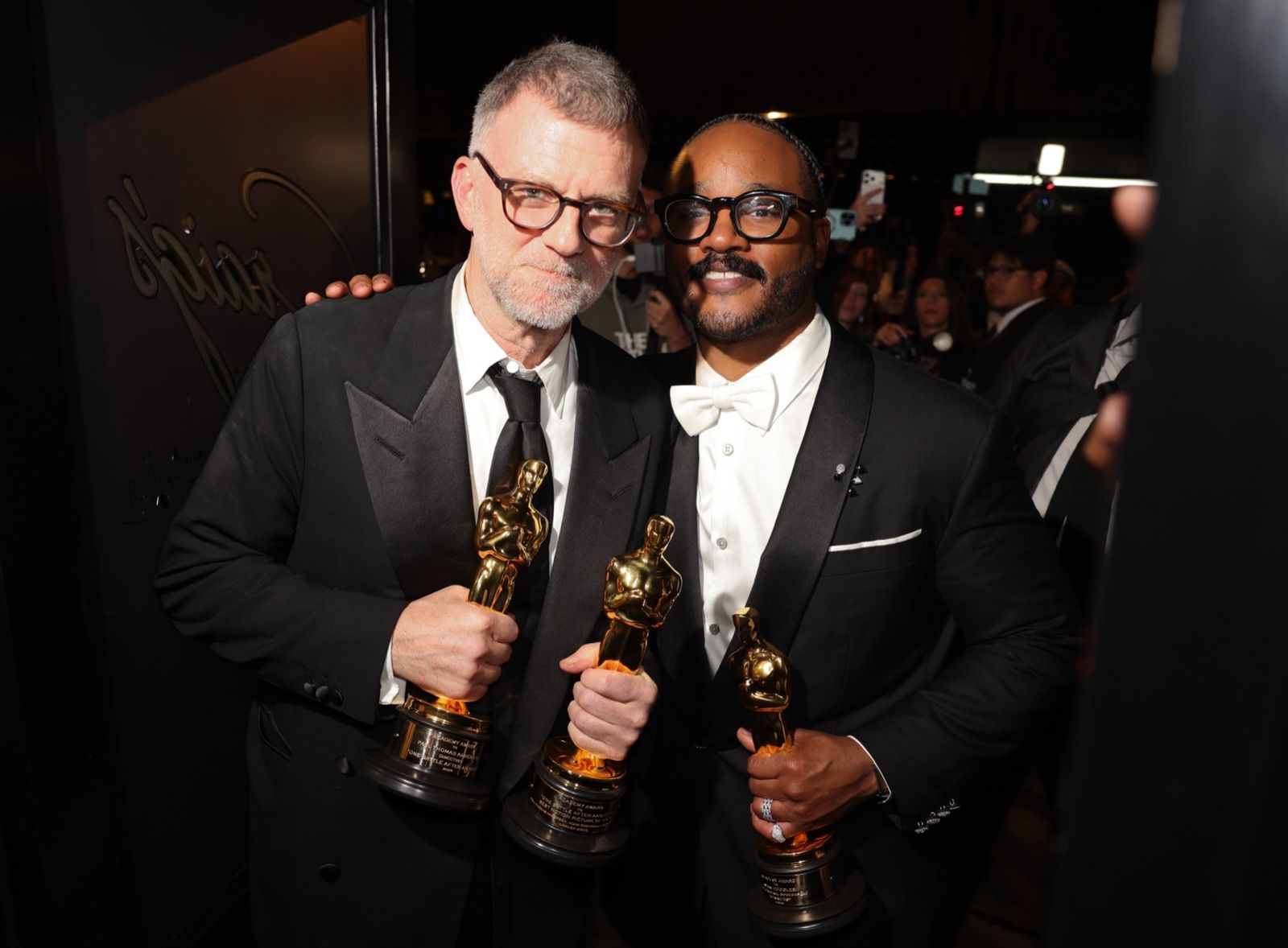 Two guests in formal wear holding Oscar statuettes at the Craig's entrance