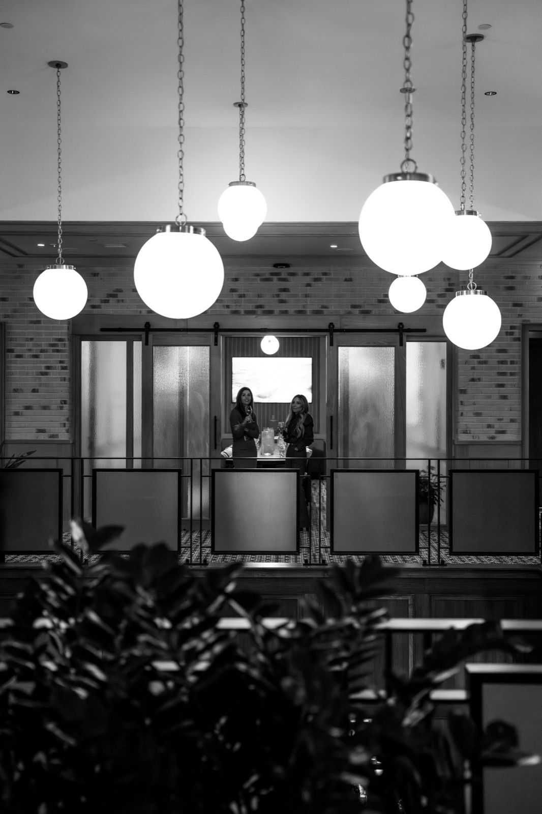 Black-and-white view of the upstairs mezzanine beneath oversized globe pendant lights
