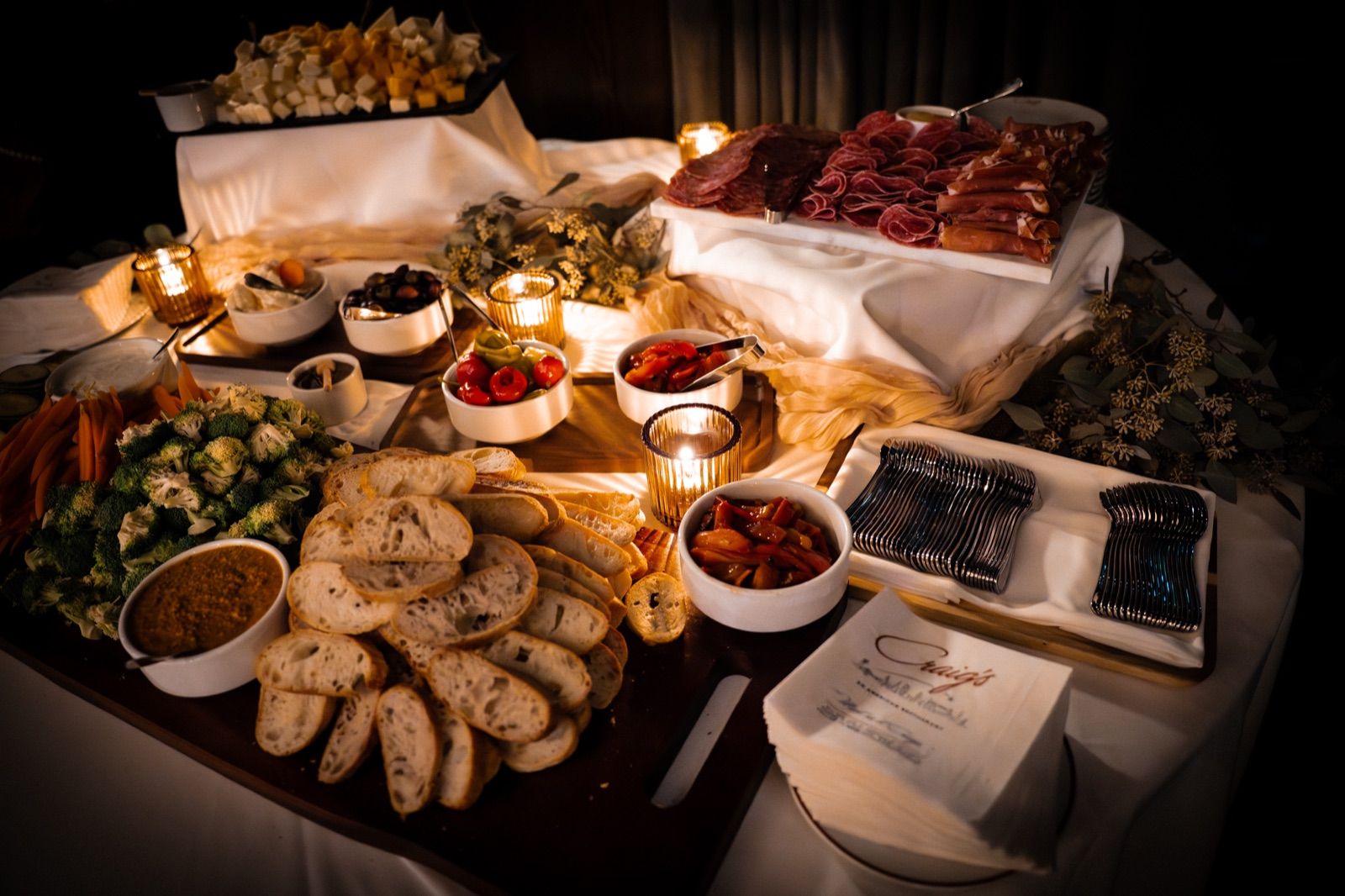 Candlelit charcuterie, bread, and antipasto spread on a draped table at a private event