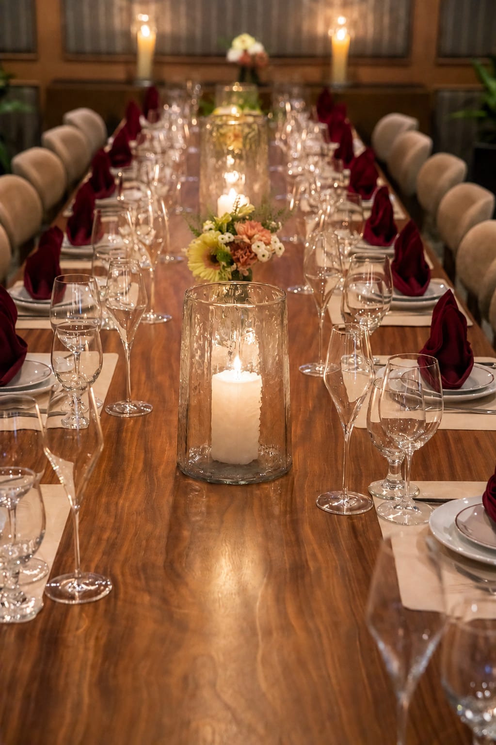 A long candlelit table dressed with burgundy napkins and fresh flowers
