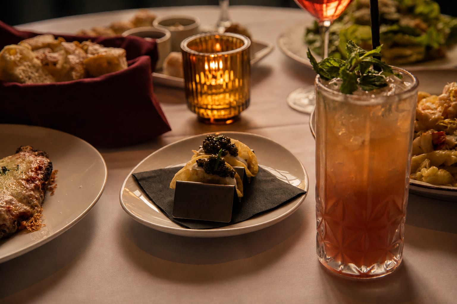 A caviar bite and a garnished cocktail on a candlelit table
