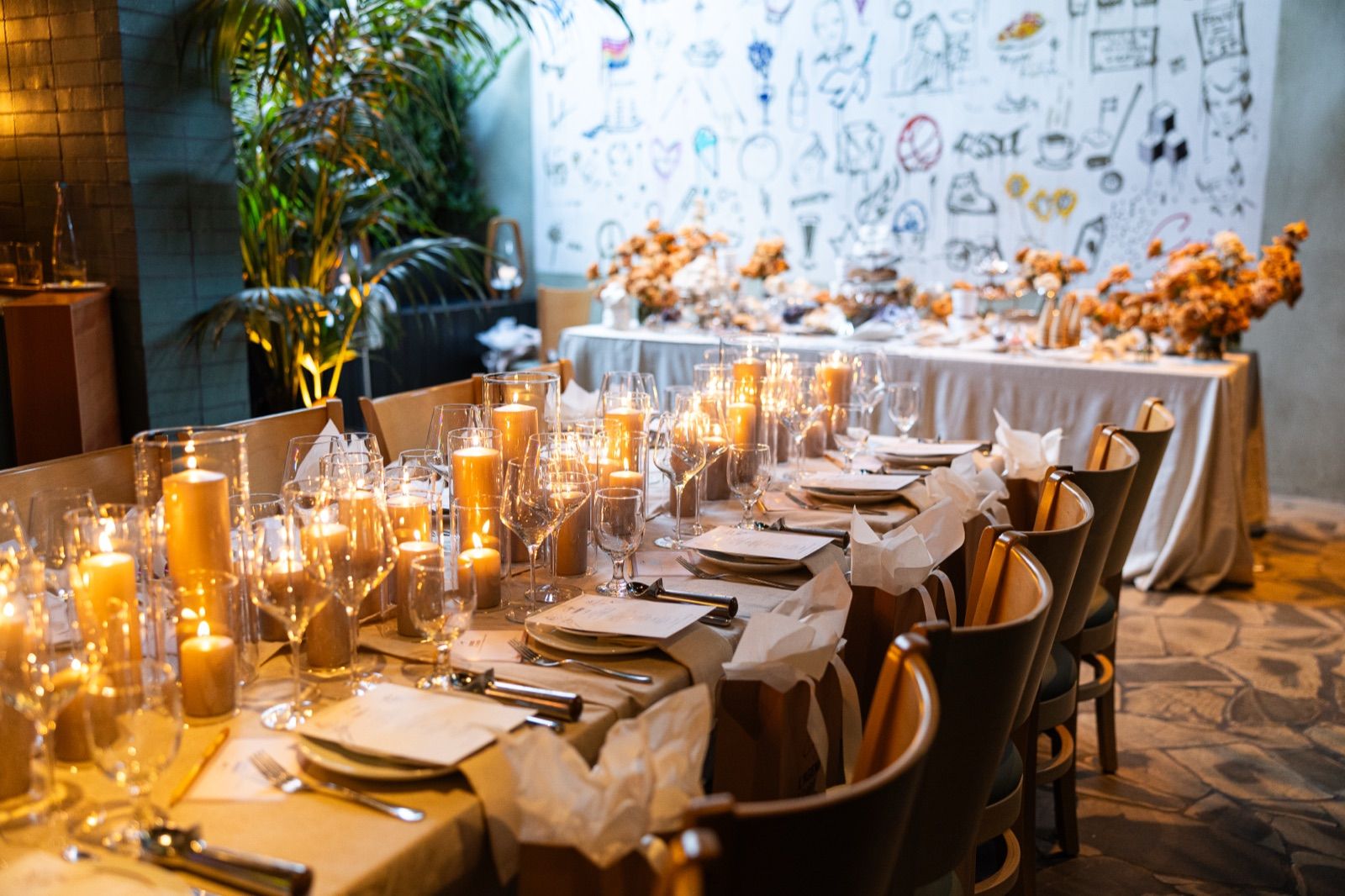 Candlelit event table with gift bags and wine glasses, dessert display and mural behind