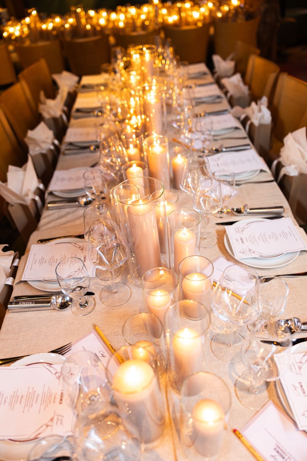 Long private dining table set with pillar-candle runners, wine glasses, and printed menus