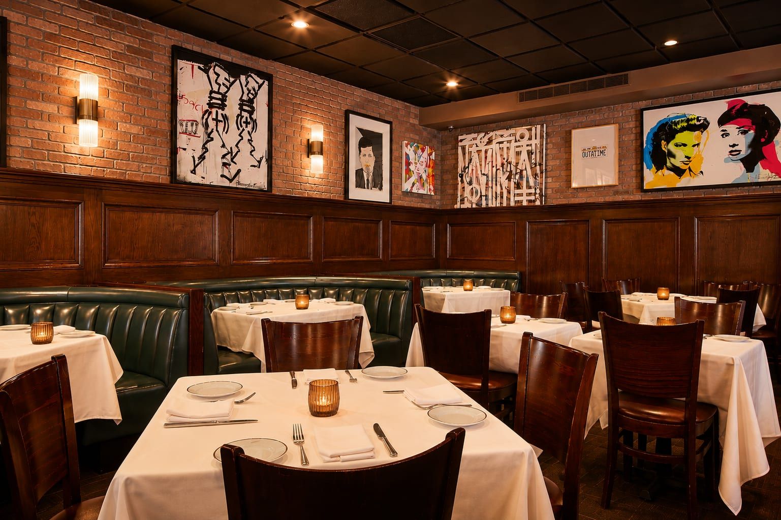 Brick-walled dining room with green leather banquettes beneath a gallery wall