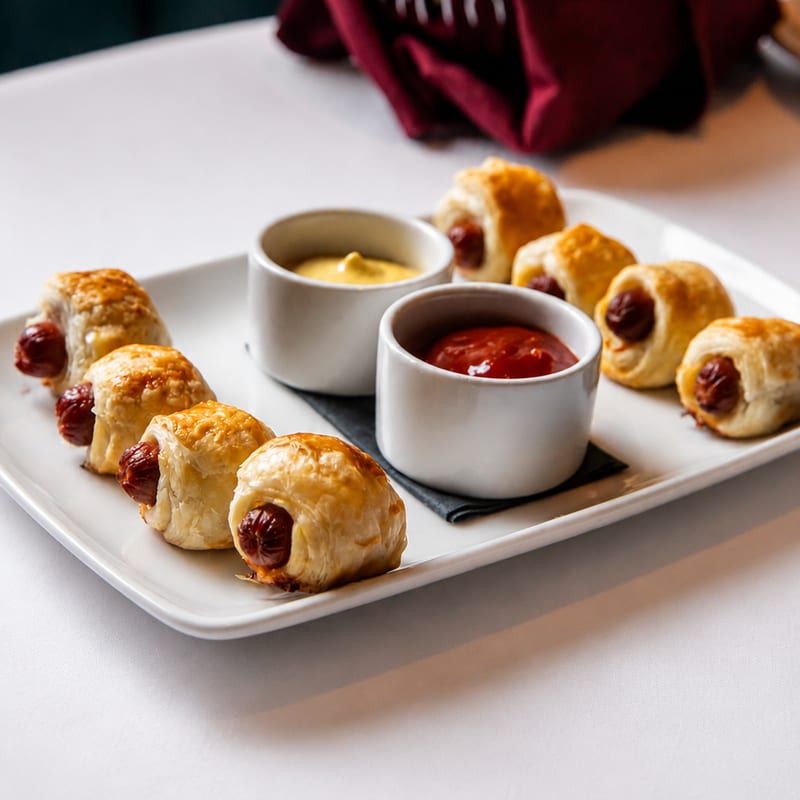 Pigs in a blanket plated with mustard and ketchup dips