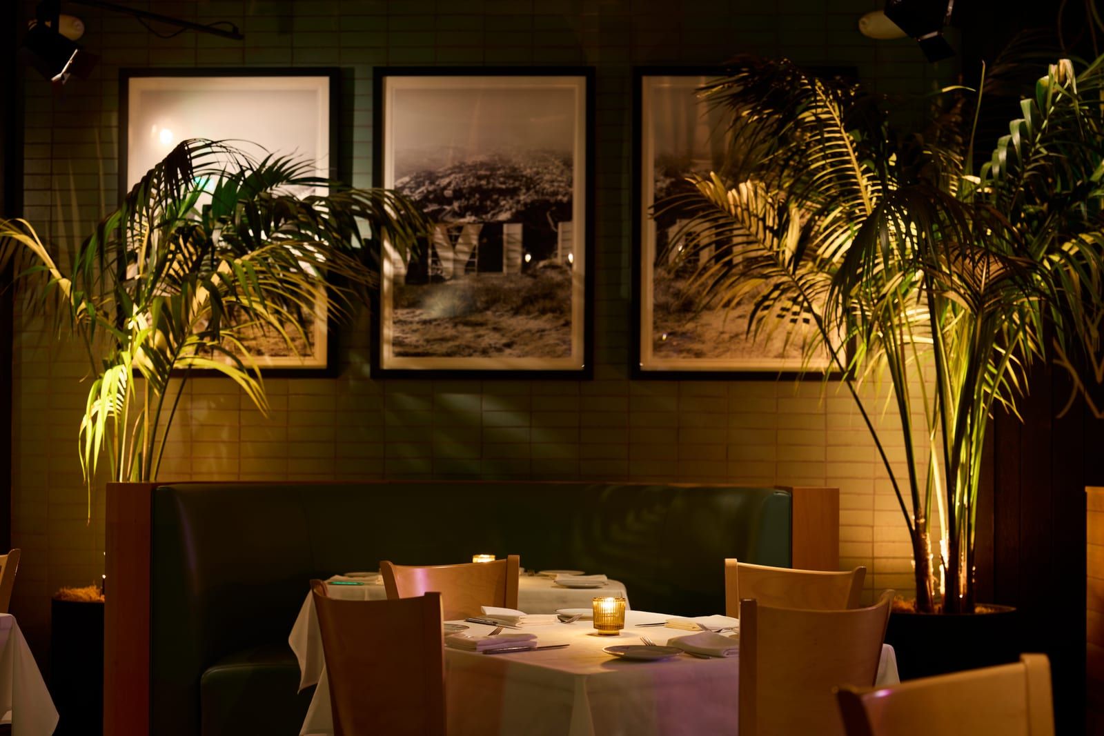 Green-tiled corner booth beneath framed black-and-white photographs and palm fronds