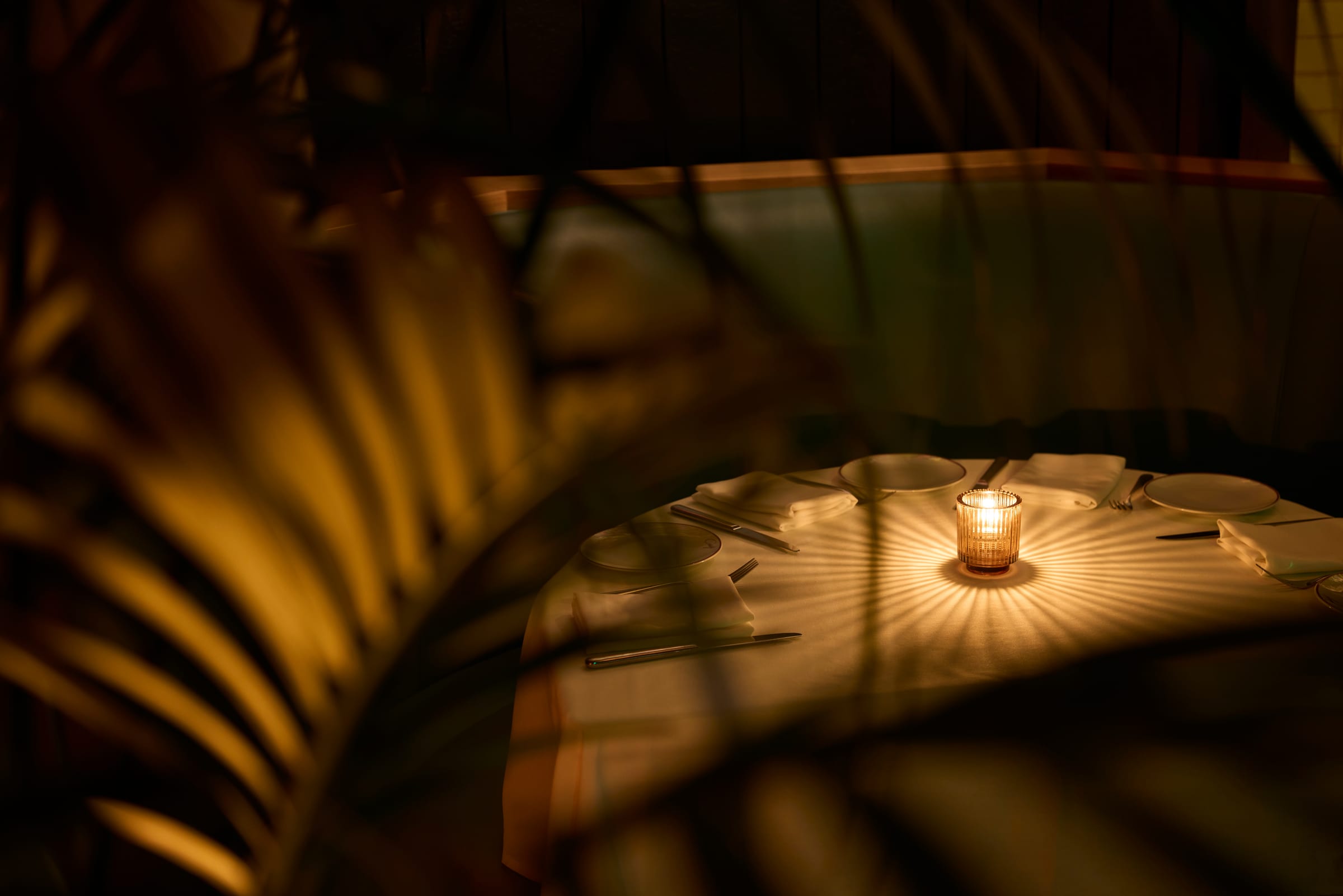 A candlelit patio table at Craig's glowing warmly behind palm fronds