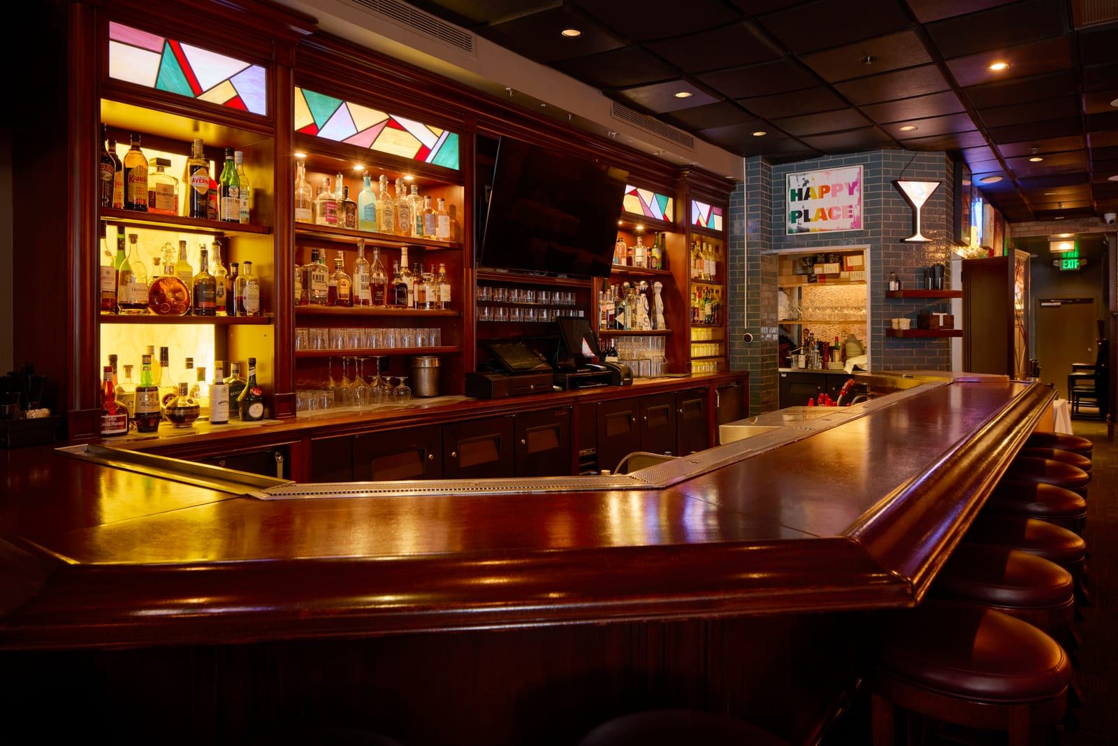 The mahogany bar beneath stained-glass panels and glowing spirit shelves
