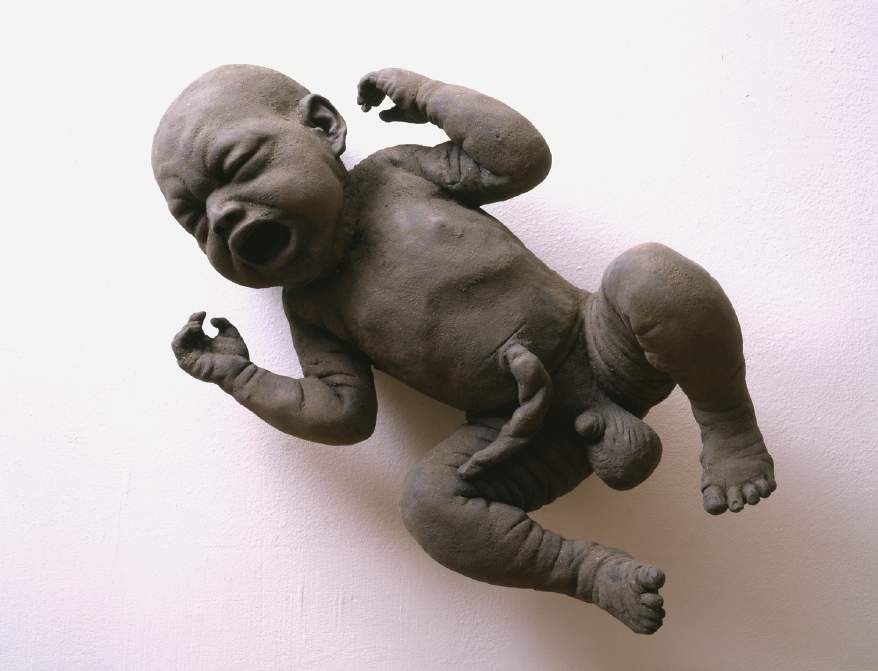 James Croak, Dirt Baby, 2000. Cast dirt sculpture of a crying baby against a white wall.