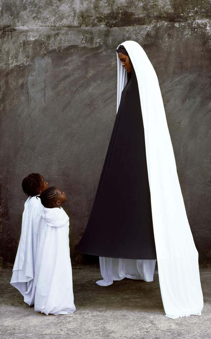 Maïmouna Guerresi, Surprise, 2010. Lambda print: a tall figure in a long white and black veil beside two small children in white.