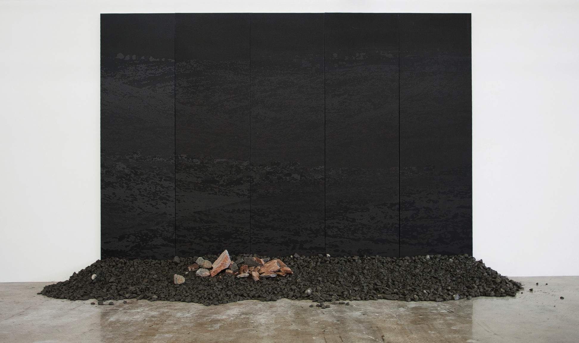 Eugene Lemay, Hezron, 2014. Installation of a digital print on canvas with granite: a large black panel above a low mound of dark stones on the gallery floor.