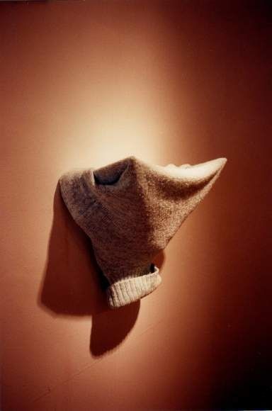 Erwin Wurm, 1991: a worn, sock-like textile form against a warm orange-brown background.