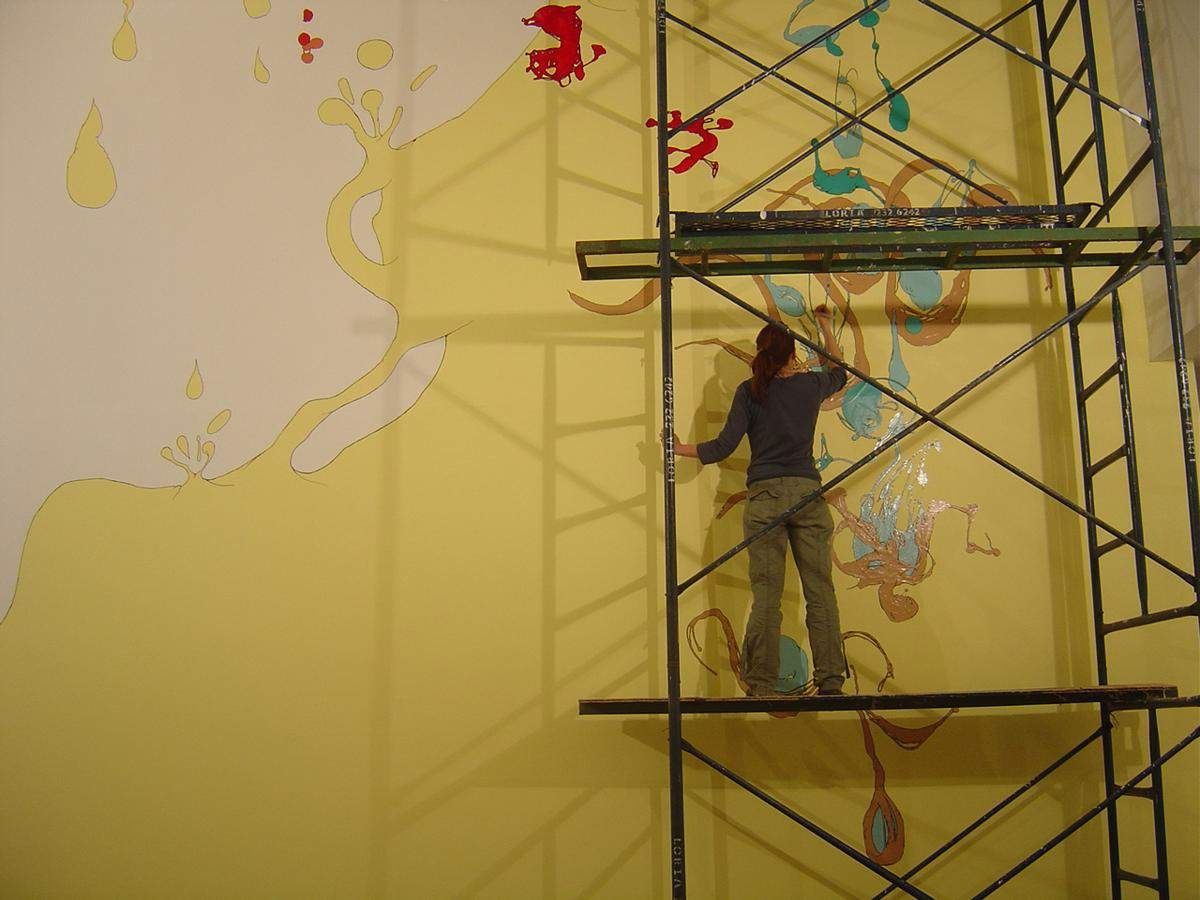 Heide Trepanier, Mural - Costa Rica: the artist on scaffolding painting a large yellow mural.