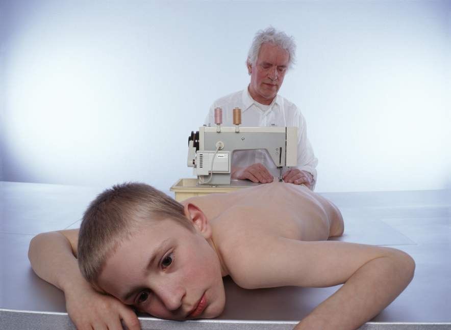 Margi Geerlinks, Pinocchio, 1999. Cibachrome: a boy lying on a table while an older man works at a sewing machine behind him.