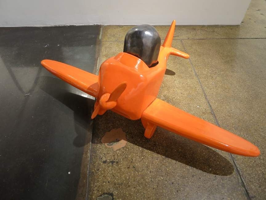 Nicolas Touron, Passenger, 2012. Ceramic sculpture of an orange, toy-like airplane on a gallery floor.