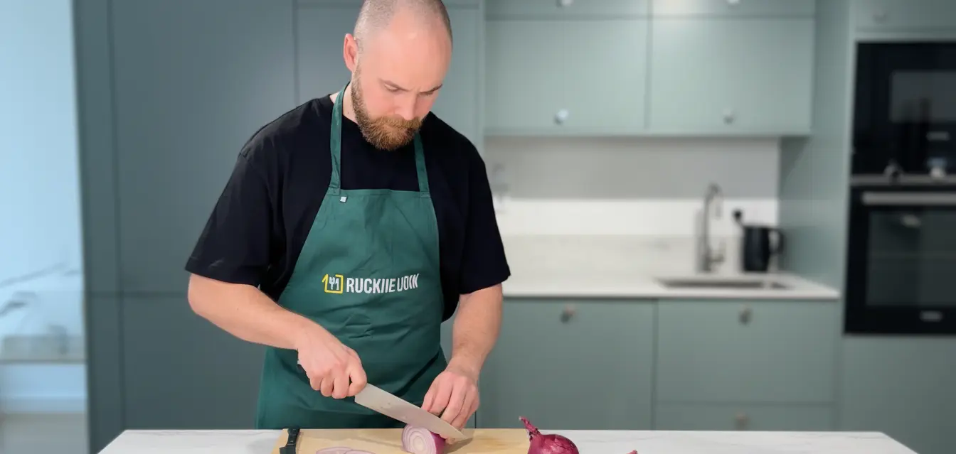 Kokki leikkaamassa sipuleita keittiössä