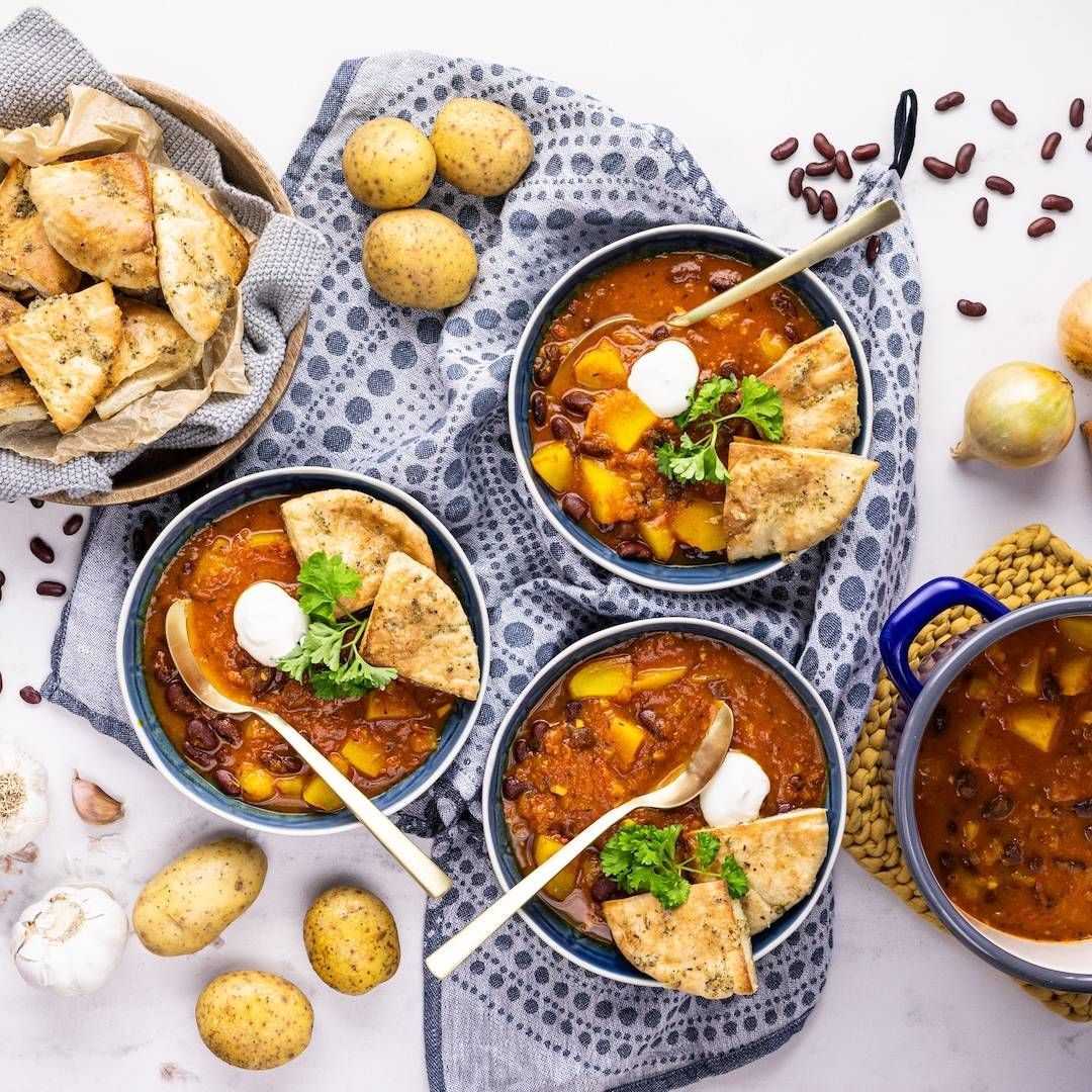Bowls of bean and potato soup with flatbread, raw potatoes and kidney beans on a table