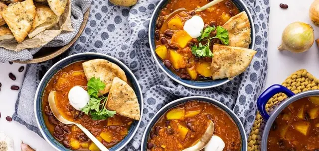 Bowls of bean and potato soup with flatbread, raw potatoes and kidney beans on a table