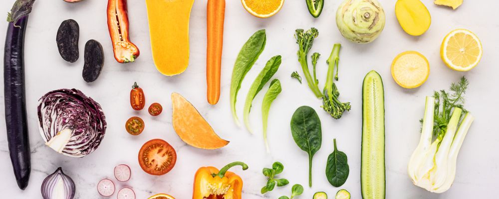 Colourful raw vegetables laid out on marble: broccolini, carrot, squash, cucumber, fennel and peppers